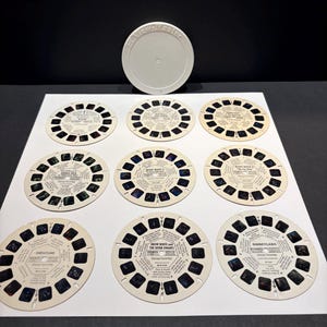 May include: A collection of nine circular View-Master reels featuring various Disney themes, including Snow White and the Seven Dwarfs, Disneyland, and Mickey Mouse, accompanied by a single white plastic View-Master storage reel cover.