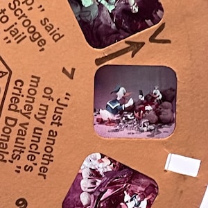 Puede incluir: Un carrete de View-Master vintage con fondo marrón e imágenes de Donald Duck y Rico McPato. El texto en el carrete dice "Pay up," said Scrooge, "to jail" y "Just another of my uncle's money vaults," cried Donald.