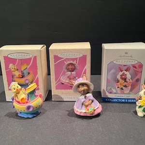 May include: Three Hallmark Keepsake ornaments in their original boxes. The ornaments are part of the Garden Club series. The first ornament is a yellow chick in a blue and white boat. The second ornament is a pink bunny in a purple dress. The third ornament is a white bunny holding a bouquet of flowers.