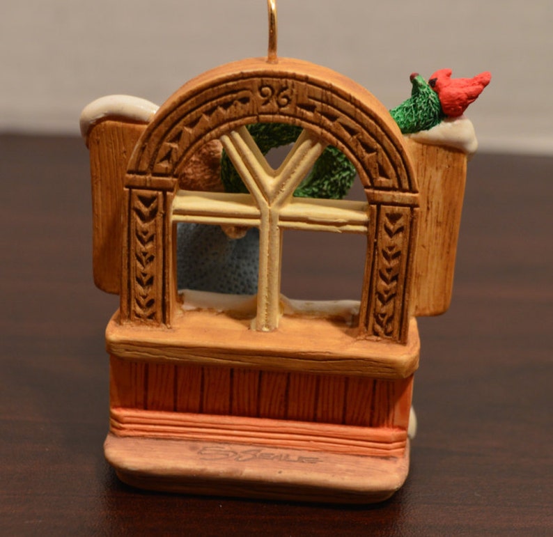 May include: A brown wooden window ornament with a white frame and a green wreath. The ornament has a red cardinal perched on top and the number "96" carved into the wood.