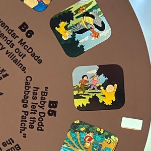May include: A brown and white circular board with colorful illustrations and text. The text reads "B5 "Baby Dodd has left the Cabbage Patch." and "B6 vendar McDade ends out zy villains."