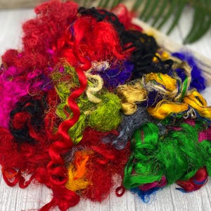 May include: A colorful mix of fibers in shades of red, green, yellow, blue, and black. The fibers are arranged in a loose pile, creating a textured and vibrant display.