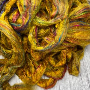 May include: A pile of golden yellow silk fiber with streaks of blue, green, and red.