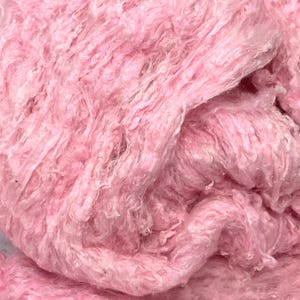 May include: A bundle of soft, light pink yarn with a highly textured, fuzzy, and irregular appearance. The fibers are loosely spun, creating a voluminous and cloud-like structure with varying thicknesses throughout the entire length of the material.