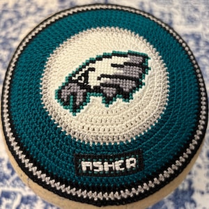 Può includere: Una kippah di uncinetto verde, bianco e grigio con un logo dei Philadelphia Eagles e la parola "Fisher" ricamata sul fondo.