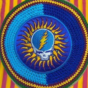 May include: A crocheted kippah with a blue and yellow Grateful Dead Steal Your Face logo patch. The kippah is made with a variety of colors, including blue, yellow, green, and maroon.