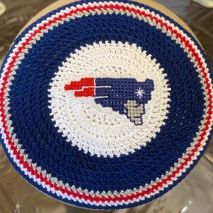 May include: A blue and white crocheted kippah with a red, white, and blue embroidered New England Patriots logo.
