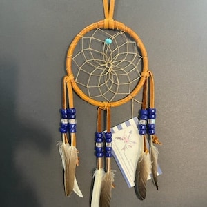 May include: A brown leather dreamcatcher with a white web and blue beads. The dreamcatcher has five feathers, two white and three brown.