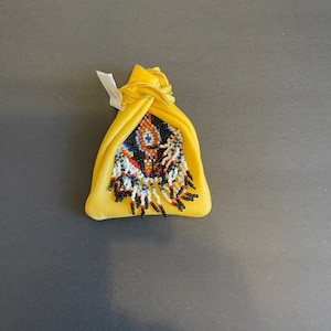 May include: A small yellow pouch with a beaded design. The pouch is tied at the top and has a fringe of beads hanging from the bottom.