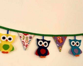 May include: A colourful owl-themed banner with green string and purple, pink, yellow, blue, and green felt owls. The owls have different patterns and designs.