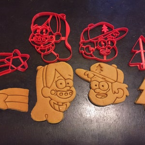 Conjunto de cortadores de biscoitos Gravity Falls. Inclui Mabel e Dipper, bem como o ícone da camisa de estrela de Mabel e o logotipo do chapéu de árvore de Dipper. Todos os 4 incluídos.