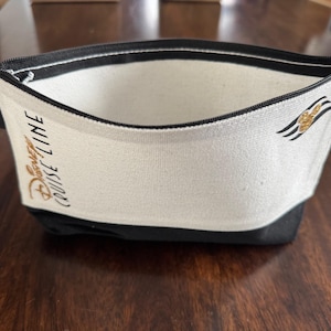 May include: A white and black zippered pouch with a gold embroidered Disney Cruise Line logo and a Mickey Mouse silhouette.