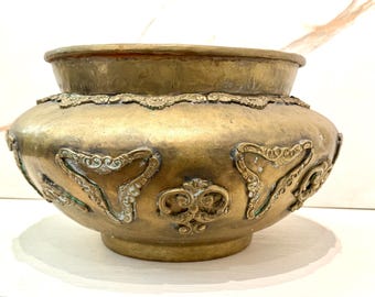 May include: A large, round, brass planter with intricate floral and geometric designs. The planter has a wide, rounded base and a slightly flared rim.