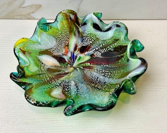 May include: A green, white, and gold glass bowl with a wavy edge. The bowl has a swirl design with flecks of silver and gold.
