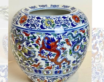 May include: A round, ceramic vase with a wide opening, featuring a detailed dragon motif. The vase is predominantly white with blue, red, yellow, and green accents. The design includes dragons, floral patterns, and intricate borders, showcasing a traditional aesthetic.