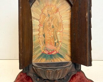 May include: A small wooden shrine with a hinged door, featuring a straw-inlaid image of the Virgin Mary. The shrine has a carved wooden base with a velvet cushion and a small, carved wooden bowl.