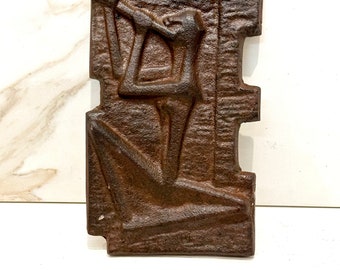 May include: A brown cast iron wall sculpture depicting a stylized human figure. The sculpture has a rough, textured surface and is in a reclining pose.