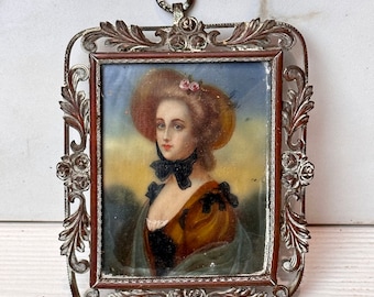 May include: A miniature portrait of a woman in a straw hat with a pink flower, wearing a brown dress with a black bow tie, framed in a silver ornate frame.