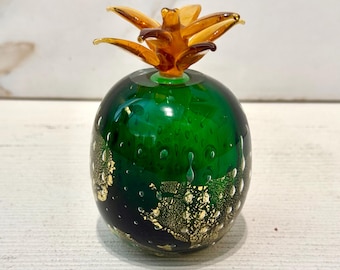 May include: A green glass pineapple with gold flecks and a brown glass top. The pineapple is a decorative object.