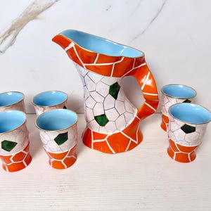 Può includere: Un brocca in ceramica e sei bicchieri abbinati. Il set presenta un design a mosaico con accenti arancioni, bianchi e verdi. Gli interni della brocca e dei bicchieri sono azzurri, con bordi dorati. Un set di stoviglie decorative.