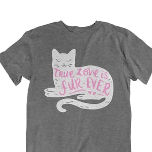 May include: A heather gray t-shirt featuring a white cat illustration with the text "True Love is Fur-Ever" in pink. The cat is lying down with its tail curled. The shirt is a casual wear item.