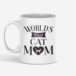 May include: White ceramic mug with a black design that reads "World's Best Cat Mom" with a pink silhouette of a cat inside a heart.