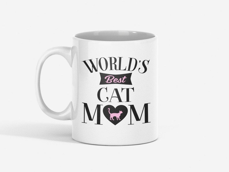 May include: White ceramic mug with a black design that reads "World's Best Cat Mom" with a pink silhouette of a cat inside a heart.