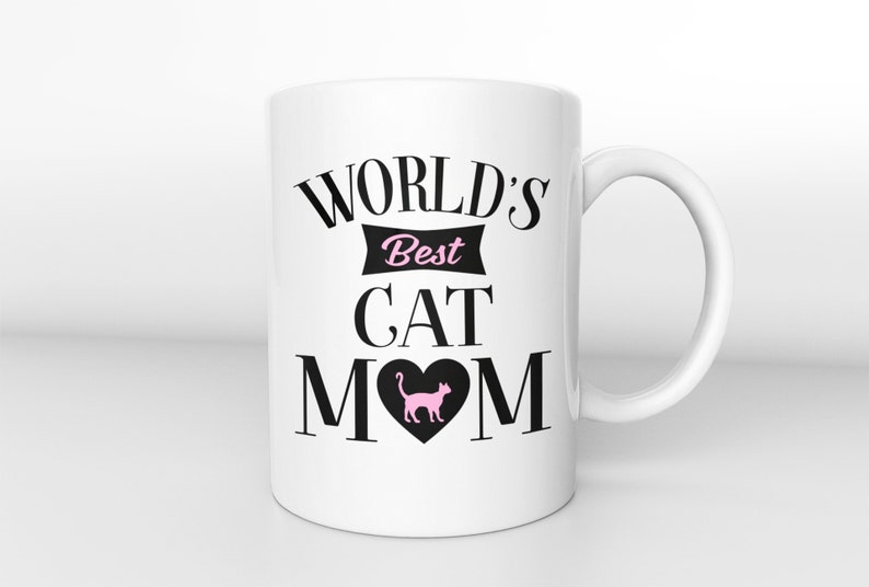 May include: White ceramic mug with black text that reads "WORLD'S Best CAT MOM" with a pink cat silhouette inside a black heart.