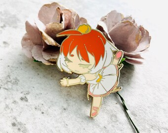 May include: Gold enamel pin featuring a cartoon ballerina with red hair, a white tutu, and a gold crown. The ballerina is in a dancing pose with one leg raised.