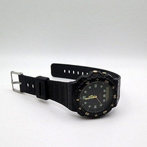May include: Black wristwatch with a black resin band and a gold-colored bezel. The watch face has a black background with gold-colored hour markers and hands.