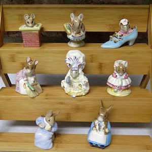 May include: A set of ten porcelain figurines of mice and rabbits, displayed on a tiered wooden shelf. The figurines are painted in various colors and depict different characters, including a mouse in a chimney, a rabbit in a blue shoe, and a mouse sweeping the floor.