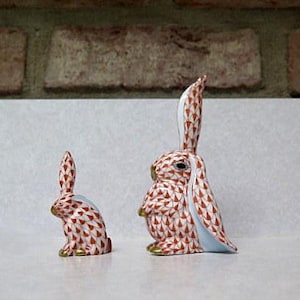 May include: Two porcelain rabbit figurines, one larger than the other. Both are white with a brown and white geometric pattern. The larger rabbit has its ears up and the smaller rabbit has its ears down.