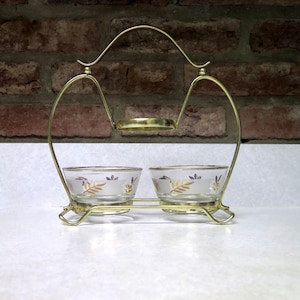 May include: A vintage gold-toned metal serving set with two small glass bowls. The bowls have a floral design with gold trim. The set includes a handle and a small tray above the bowls.