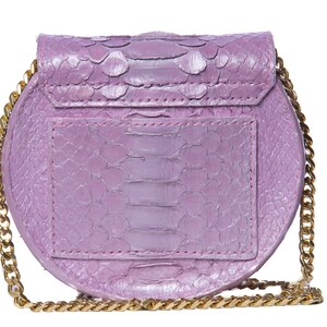 Pu&ograve; includere: Una piccola borsa rotonda di colore lavanda con una tracolla a catena dorata. La borsa &egrave; realizzata in pelle di serpente e ha una chiusura a lembo.
