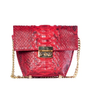 May include: A red snakeskin crossbody bag with a gold chain strap and a gold lock closure.