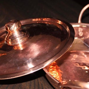 May include: A copper pot with a hammered finish and a lid with a knob. The pot has a handle on each side.