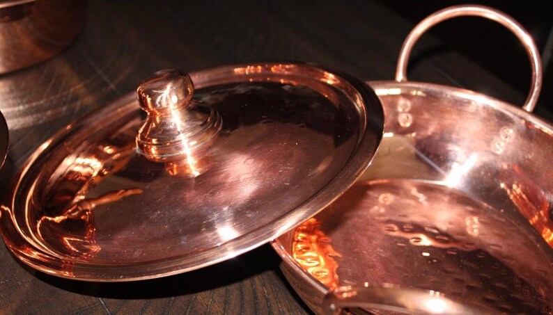 May include: A copper pot with a hammered finish and a lid with a knob. The pot has a handle on each side.