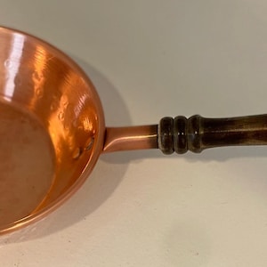 May include: A copper frying pan with a wooden handle. The pan has a hammered finish and is in good condition.