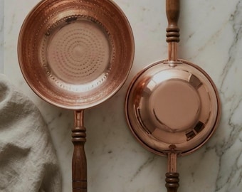 May include: Two copper pans with dark wooden handles and metal hanging loops. One pan shows the interior with a hand-hammered texture, while the other shows the smooth exterior base. Text reads: Hand-Hammered Strength. Engineered for flawless heat distribution on any standard residential burner.