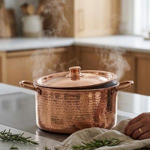 May include: A white ceramic mug with a black handle and the text "But First, Coffee" in a bold, black font. The mug is set against a blurred background, suggesting a cozy setting.