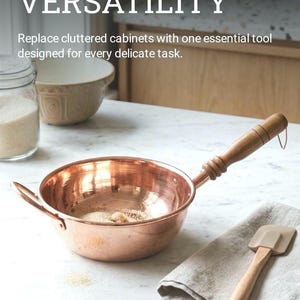 May include: A copper-colored pan with a wooden handle sits on a marble countertop. The pan contains sugar. A beige spatula and a linen towel are next to the pan. The text "EFFORTLESS VERSATILITY" is at the top of the image.