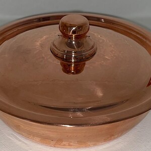 May include: A copper serving dish with a lid and two handles. The dish is round and has a shiny finish.