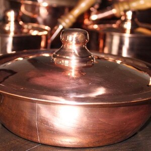 May include: A set of copper cookware with a lid. The cookware is shiny and has a traditional design.