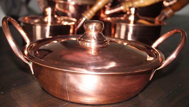 May include: A set of copper cookware with a lid. The cookware is shiny and has a traditional design.