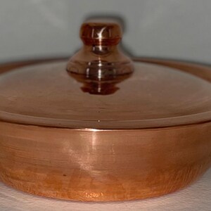 May include: A copper pot with a lid and two handles. The pot is round and has a hammered finish. The lid has a knob on top.