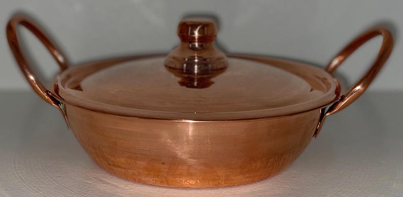 May include: A copper pot with a lid and two handles. The pot is round and has a hammered finish. The lid has a knob on top.