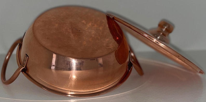May include: A copper pot with a lid and two handles. The pot is shiny and has a rounded bottom.