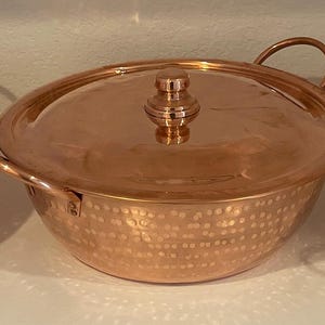 May include: Three copper serving bowls with lids. The bowls have a hammered texture and are oval shaped. Each bowl has a knob on the lid.