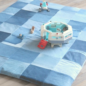 May include: A patchwork play mat made from various shades of blue denim. The mat is square and features a grid pattern. Toy spaceship, space station, and other toys are on the mat.