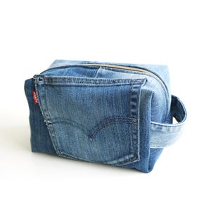May include: A blue denim zippered pouch with a handle. The pouch is made from recycled denim jeans, featuring a back pocket and the red Levi's tag. The zipper is gold-colored.